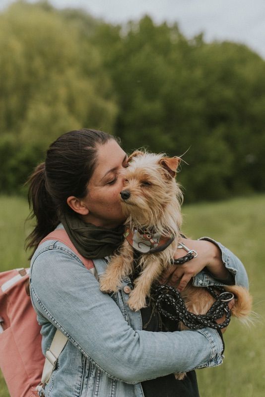 Junge Frau hält kleinen Hund auf dem Arm und drückt ihr Gesicht in sein Fell