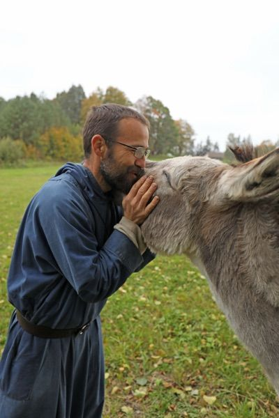 Friar in blue habit caresses a donkey that stretches its head towards him