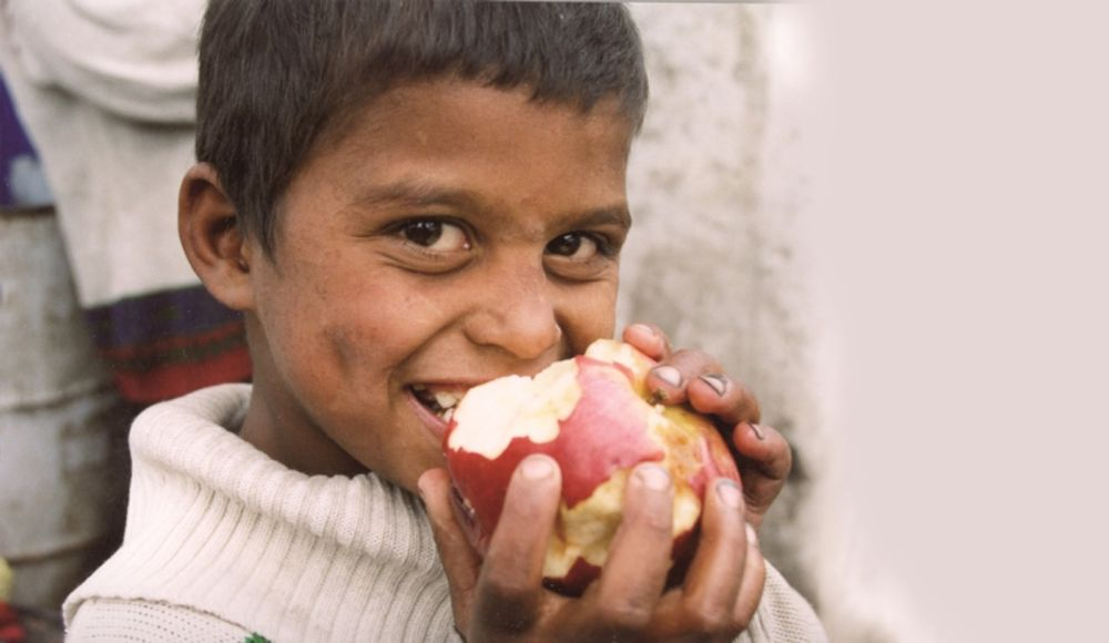 Little Roma boy takes a hearty bite of a big red apple