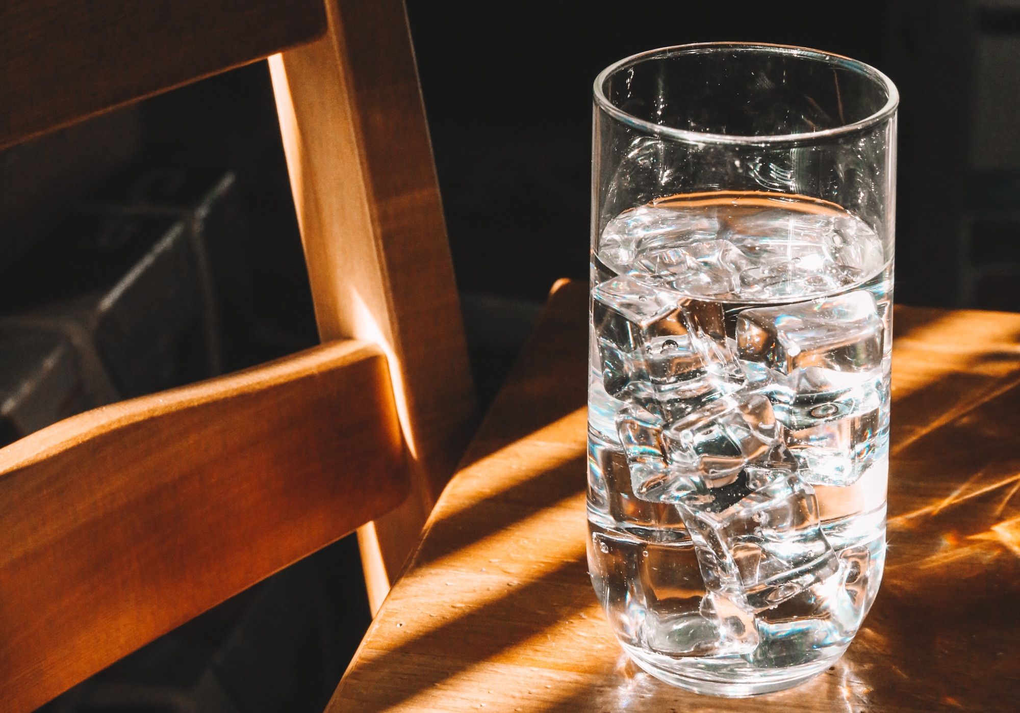 Glas mit Wasser und Eiswürfeln auf einem Tisch im Sonnenlicht